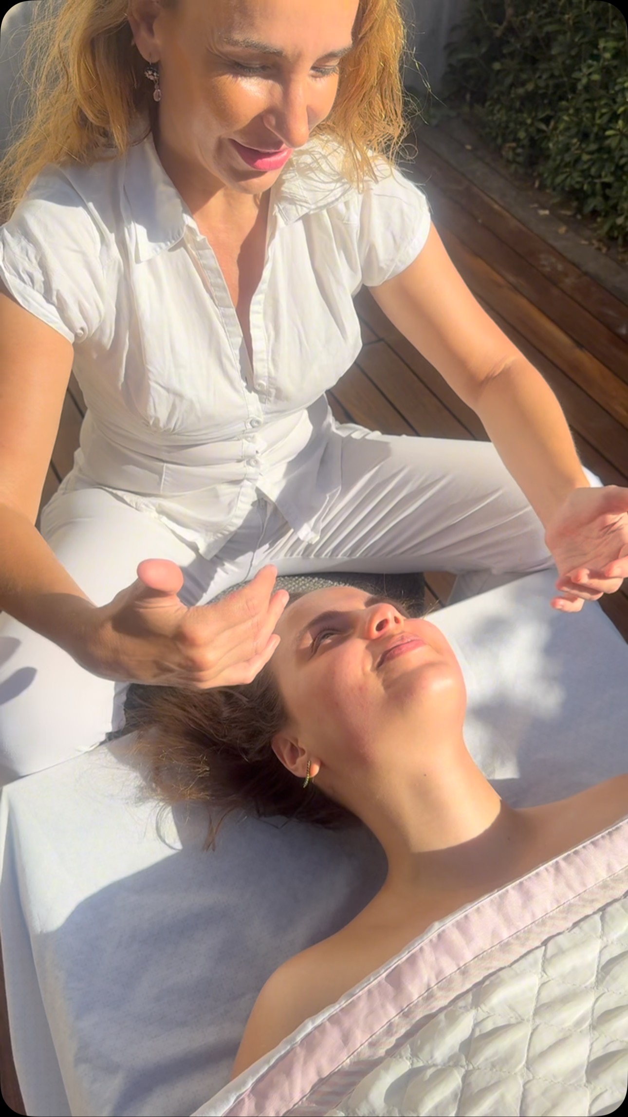 Verónica, de blanco, trabaja con las manos sobre el rostro de una clienta recostada en un deck al sol